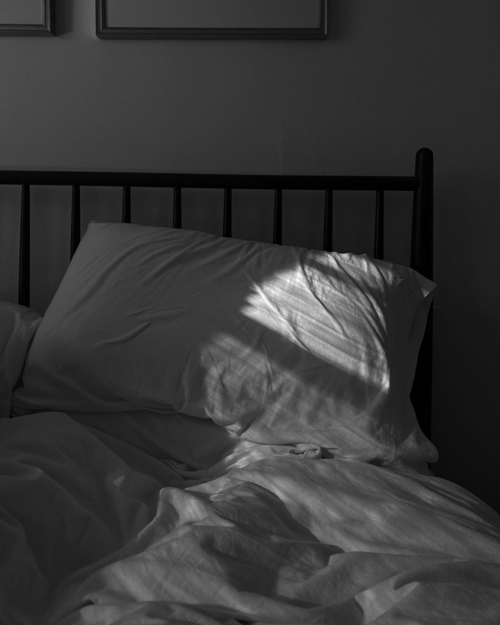 The sun casts light across a pillow on an unmade bed in the morning.