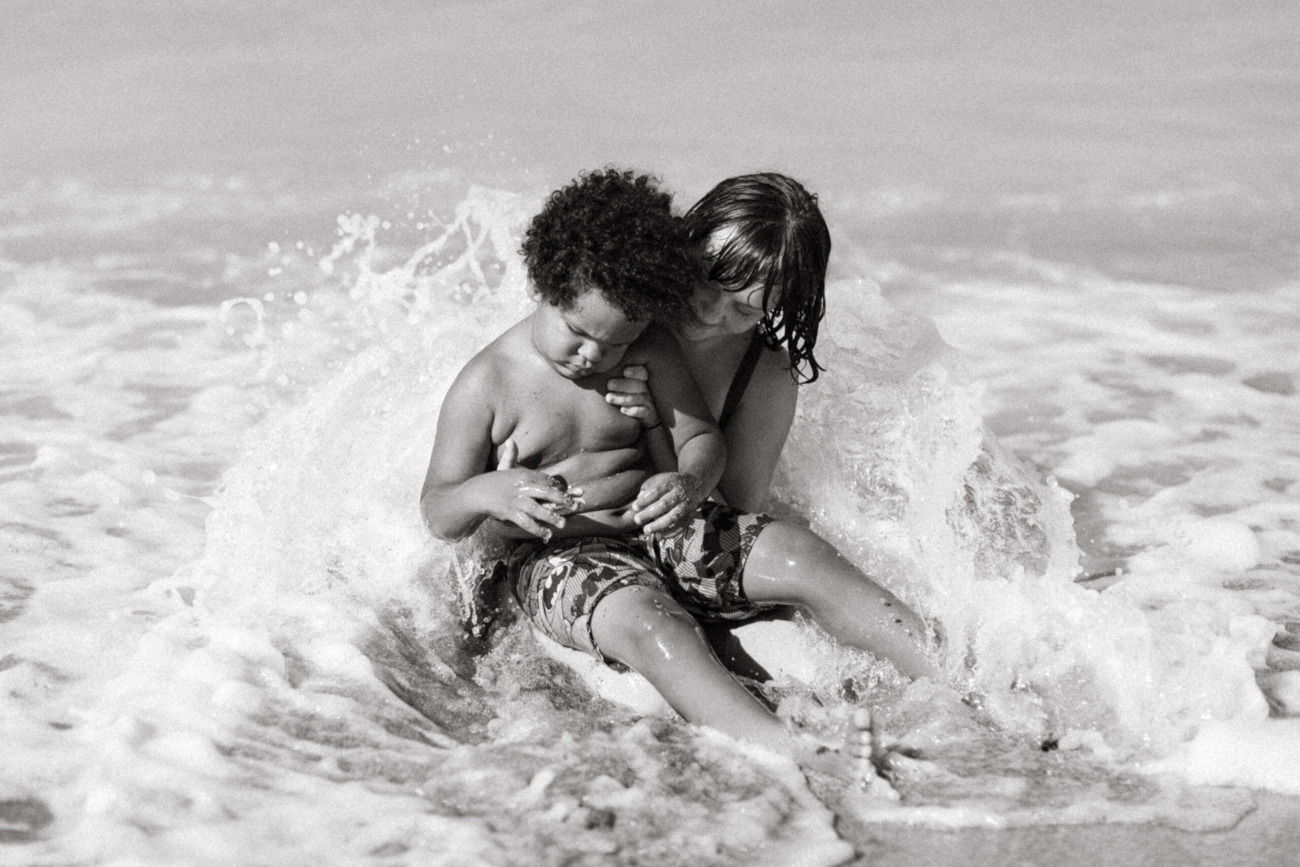 Black and white photo of a sister holding her brother in the ocean