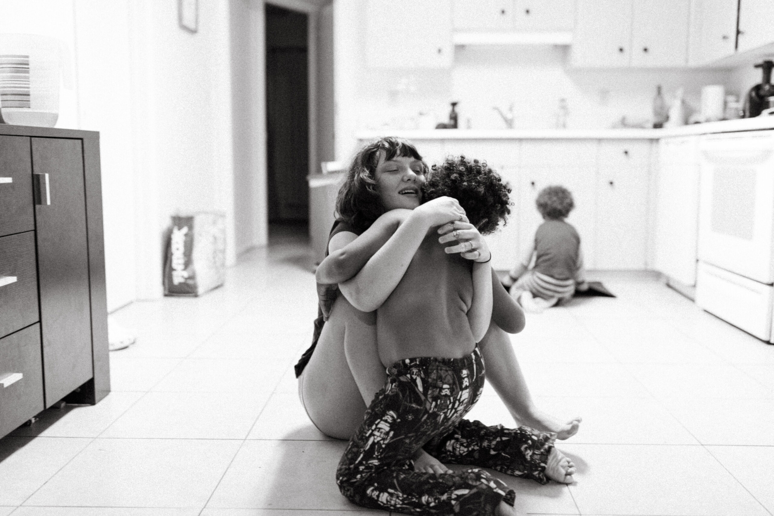 Lifestyle Family Photographer from Cincinnati, Ohio Sister hugs her brother on the kitchen floor