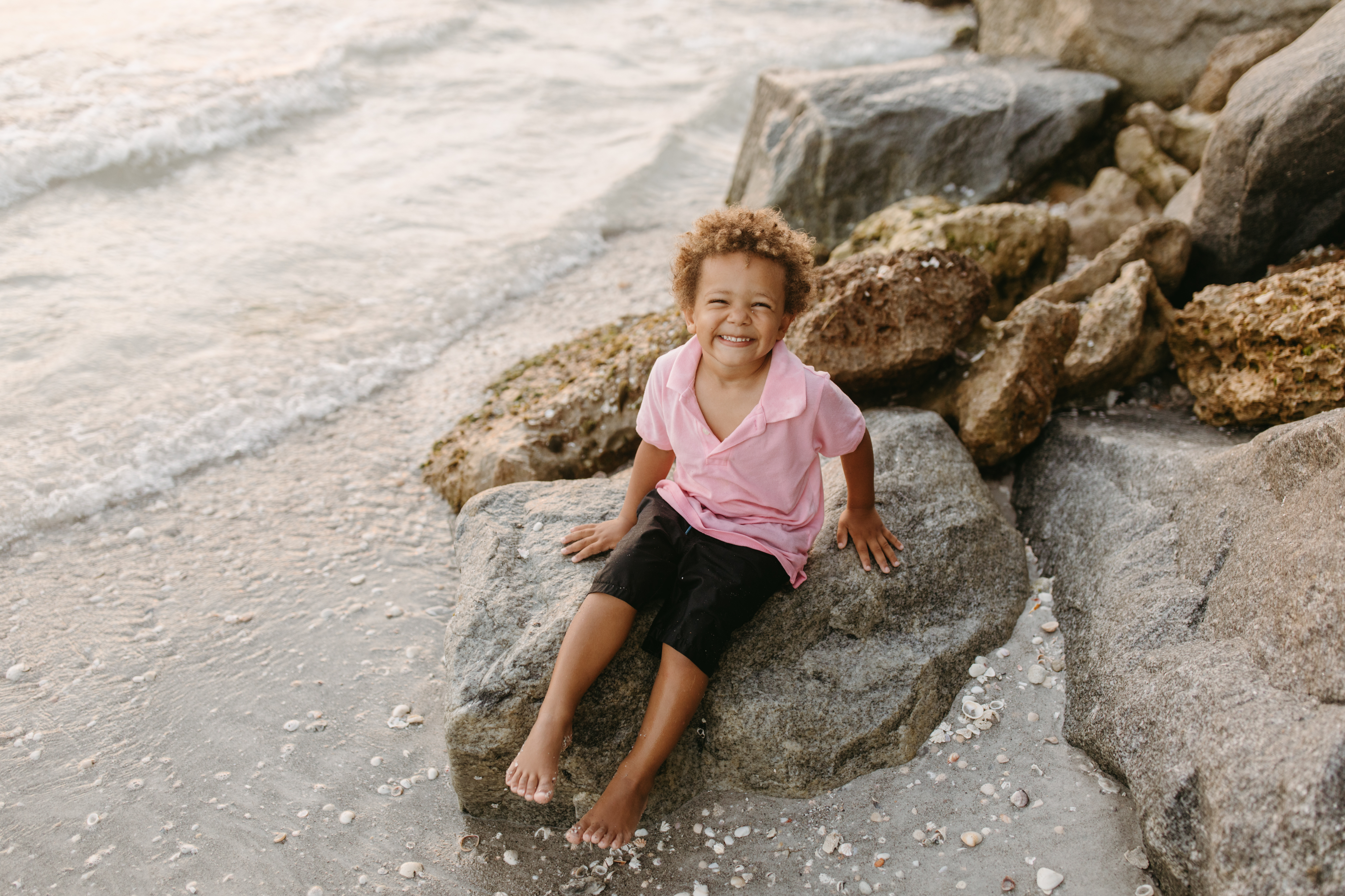 Little boy sits on a rock by the ocean at sunset